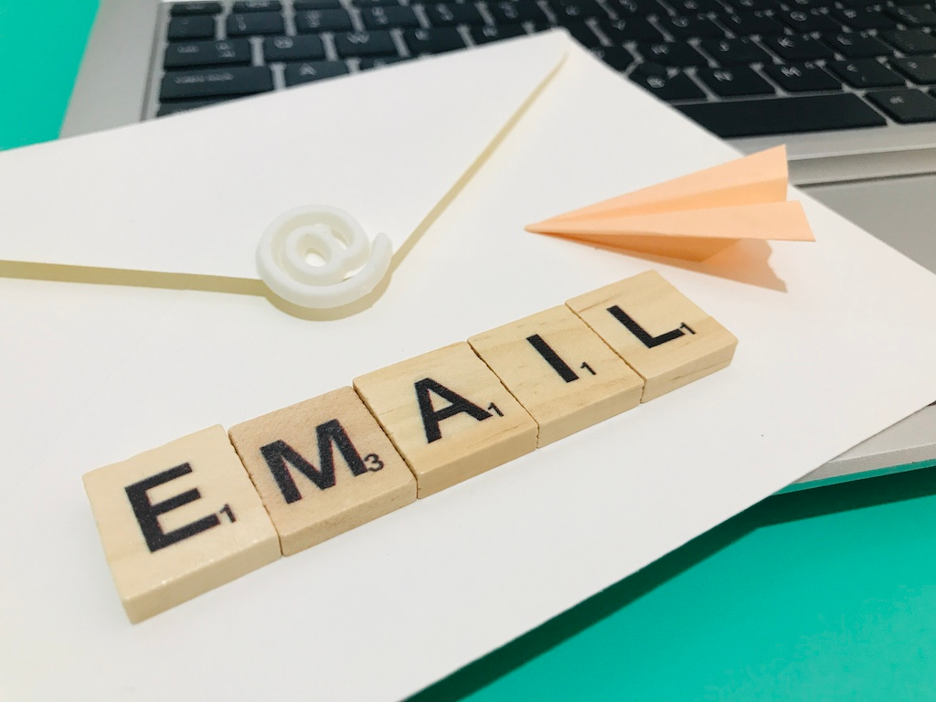 The word EMAIL written in scrabble tiles on an envelope with an @ symbol and a paper plane, signifying concept of sending email