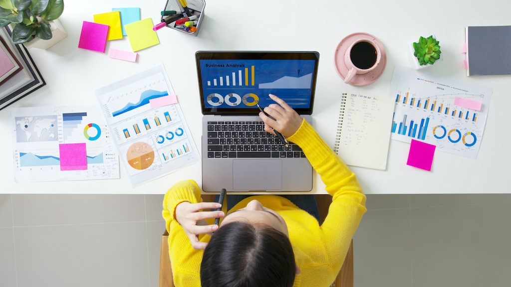 View from above of enterprise business analyst tracking digital marketing activities in graphs on a laptop screen