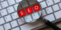 Magnifying glass signifying search concept over keyboard highlighting letters SEO in red